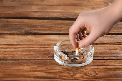 Man putting out cigarette in ashtray on wooden table, closeup. Space for text