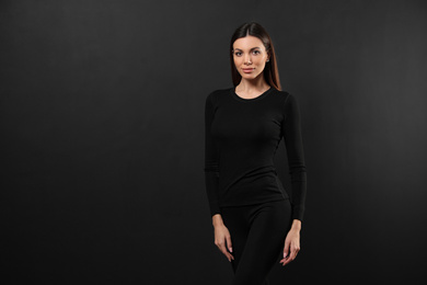 Woman wearing thermal underwear on black background. Space for text