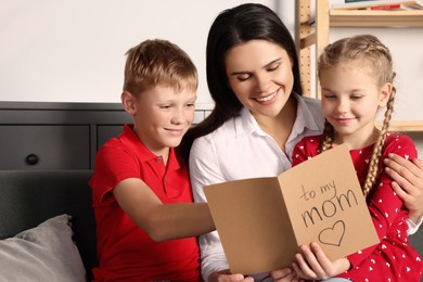 Happy woman receiving greeting card from her children at home
