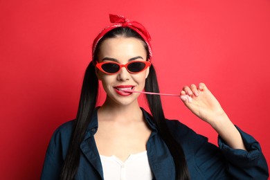 Fashionable young woman in pin up outfit chewing bubblegum on red background