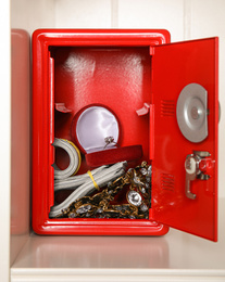 Open red steel safe with money and jewelry on shelf