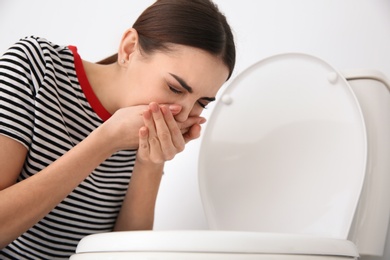 Young woman suffering from nausea at toilet bowl indoors