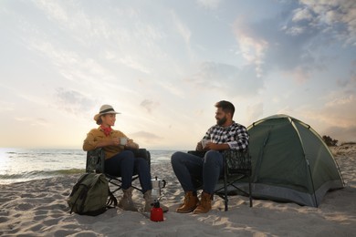 Couple with hot drinks near camping tent on beach