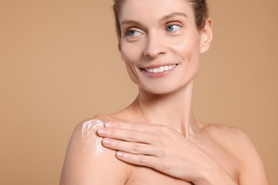 Photo of Woman applying body cream onto her arm against beige background, closeup. Space for text