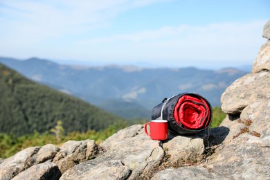 Sleeping bag and cup on mountain peak, space for text