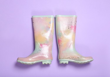 Pair of colorful rubber boots on violet background, top view