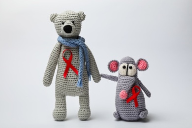 Cute knitted toys with red ribbons on light grey background. AIDS disease awareness