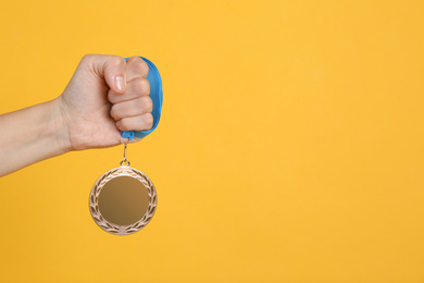 Woman holding bronze medal on yellow background, closeup. Space for design