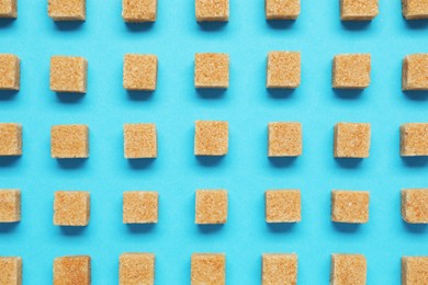 Brown sugar cubes on turquoise background, flat lay