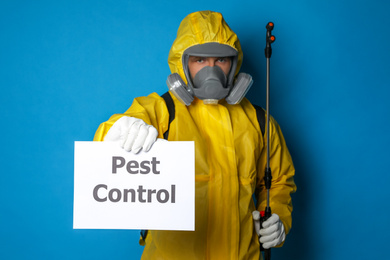 Man wearing protective suit with insecticide sprayer holding sign PEST CONTROL on blue background