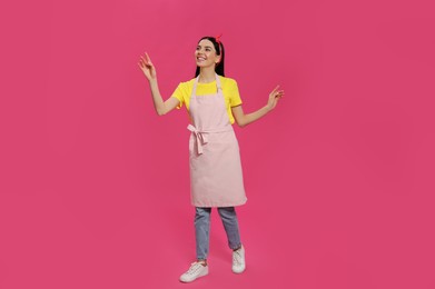Photo of Young housewife wearing apron on pink background