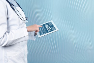 Doctor holding modern tablet with word Candida on light blue background, closeup