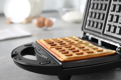 Photo of Modern iron with tasty Belgian waffles on grey table, closeup