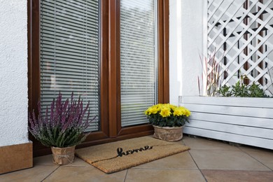 Photo of Doormat with word Home and flowers near entrance outdoors
