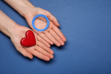 Woman showing blue paper circle as World Diabetes Day symbol and red heart on color background, top view with space for text