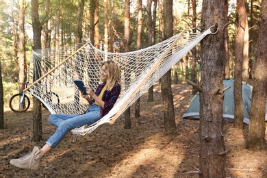 Beautiful young woman with book relaxing in hammock outdoors on summer day
