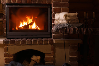 Stack of knitwear near fireplace with burning wood indoors. Winter vacation