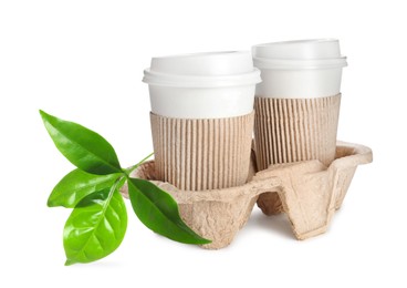 Image of Takeaway paper coffee cups with sleeves in cardboard holder and green leaves on white background. Eco friendly lifestyle