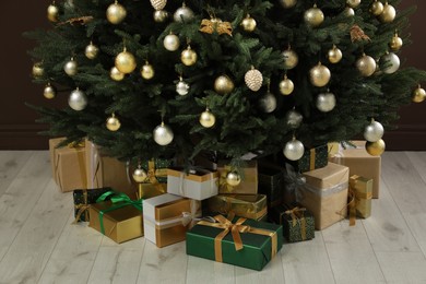 Beautifully decorated Christmas tree and many gift boxes near brown wall indoors, closeup