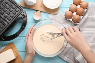 Photo of Woman preparing dough for Belgian waffles at light blue wooden table, top view