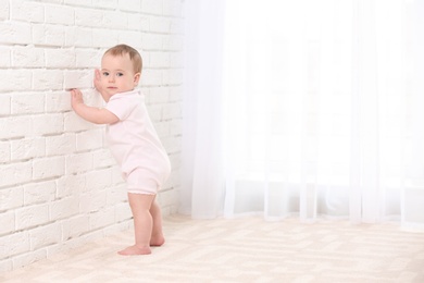 Cute baby holding on to wall indoors. Learning to walk