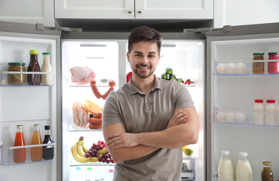Young man near open refrigerator in kitchen