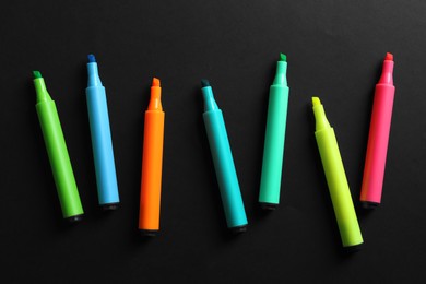 Many colorful markers on black background, flat lay. School stationery
