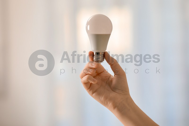 Woman holding fluorescent light bulb on blurred background, closeup. Saving energy concept