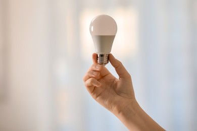 Photo of Woman holding fluorescent light bulb on blurred background, closeup. Saving energy concept