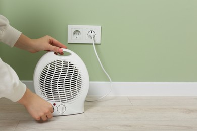 Photo of Woman turning on electric fan heater indoors, closeup. Space for text