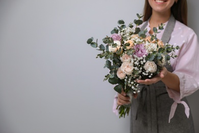 Florist holding beautiful wedding bouquet on light grey background, closeup. Space for text