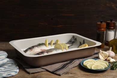 Photo of Baking tray with raw sea bass fish and ingredients on wooden table