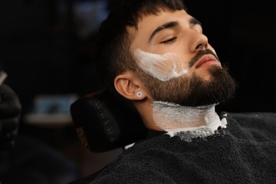 Bearded client with shaving foam on face in barbershop, closeup