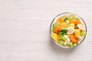 Delicious fresh fruit salad in bowl on white wooden table, top view. Space for text