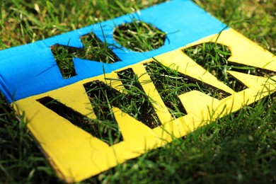 Photo of Poster in colors of Ukrainian flag with words No War on green grass, closeup