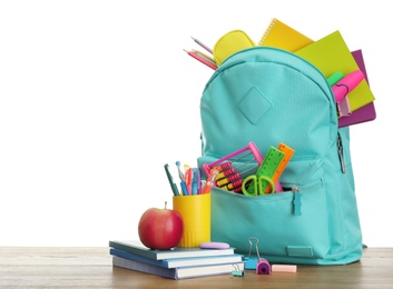 Stylish backpack with different school stationary and apple on wooden table against white background