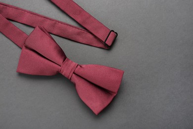 Stylish burgundy bow tie on dark background, top view. Space for text