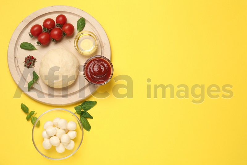 Photo of Raw dough and other pizza ingredients on yellow background, flat lay. Space for text