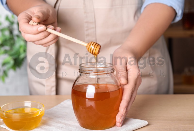 Photo of Woman with tasty honey at wooden table, closeup