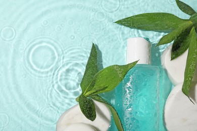 Wet bottle of micellar water, cotton pads and green twigs on light blue background, flat lay. Space for text