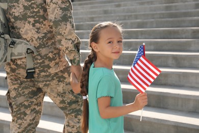 Soldier and his little daughter with American flag outdoors. Veterans Day in USA