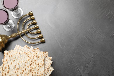 Stack of traditional matzos, red wine and menorah on grey table, flat lay. Space for text