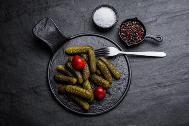 Serving board with pickled cucumbers and peppers on black table, flat lay