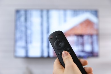 Woman with remote control watching TV at home, closeup. Space for text
