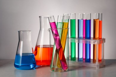 Photo of Different laboratory glassware with colorful liquids on wooden table against grey background