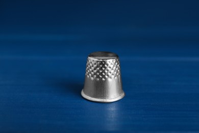 Photo of Silver thimble on blue wooden table. Sewing accessory