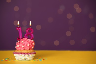 Coming of age party - 18th birthday. Delicious cupcake with number shaped candles on yellow table against blurred lights, space for text