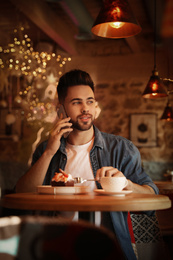 Young blogger talking on phone at table in cafe