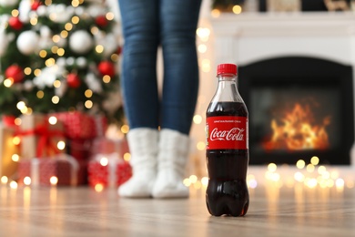 Photo of MYKOLAIV, UKRAINE - JANUARY 15, 2021: Woman in room decorated for Christmas, focus on Coca-Cola bottle
