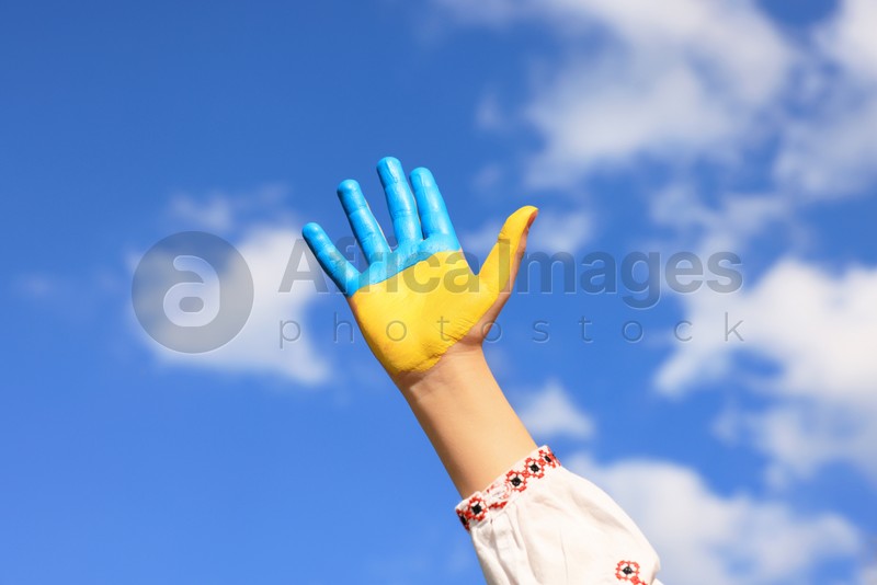Photo of Little girl with hand painted in Ukrainian flag colors against blue sky, closeup. Love Ukraine concept